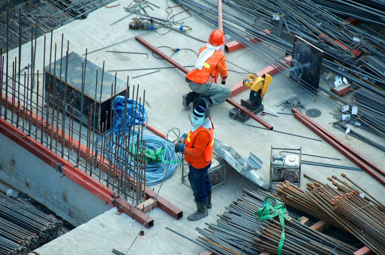 Tradespeople in high-visibility vests working on a concrete slab with steel and tools